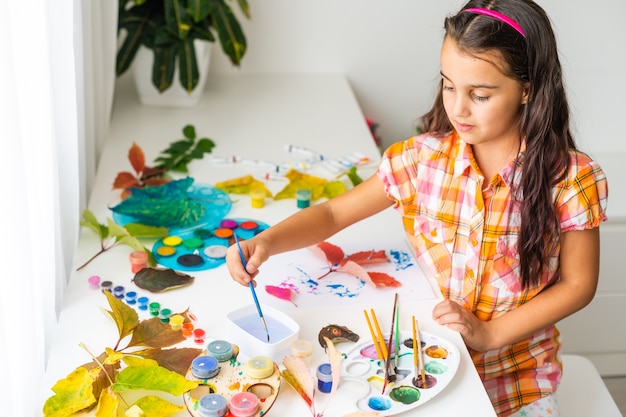 写真 ガッシュ、子供の芸術、子供の創造性、秋の芸術で秋の黄色の葉に絵を描く少女。