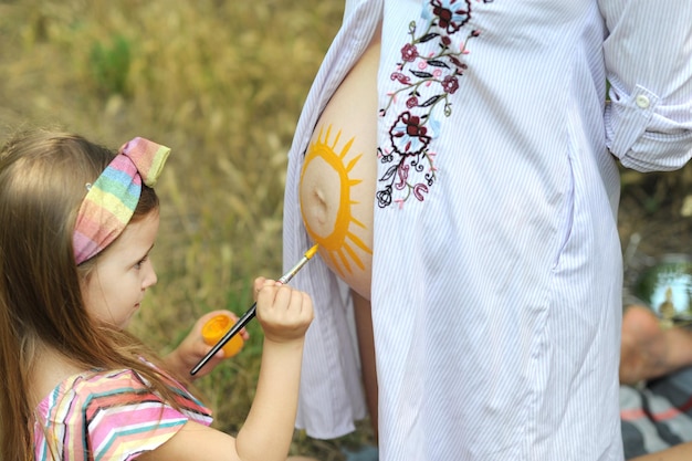 Маленькая девочка рисует солнце на животе беременной мамы