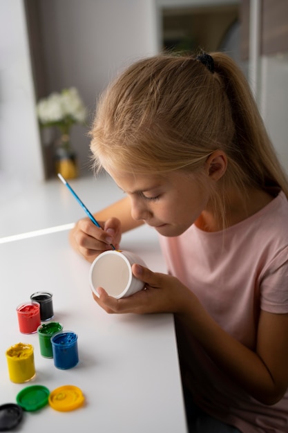 Little girl painting vase at home