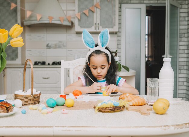 Little girl paints easter eggs Happy family is preparing for Easter Cute little girl with bunny ears on Easter day