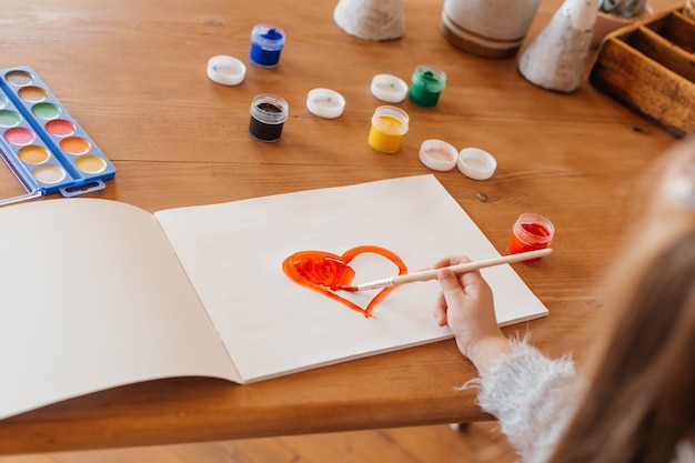 Little girl paints a heart at the table in the living room