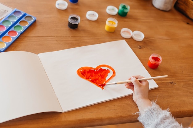 Little girl paints a heart at the table in the living room