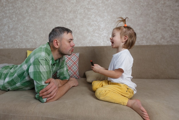 A little girl paints her lips with bright lipstick to her father