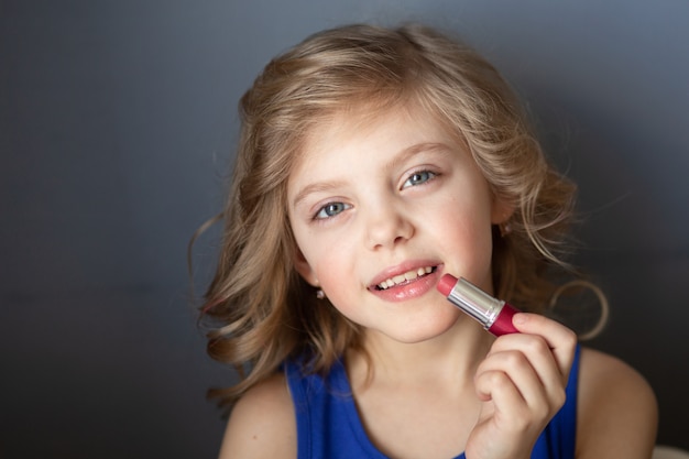 Photo little girl paints her lips with mom’s lipstick