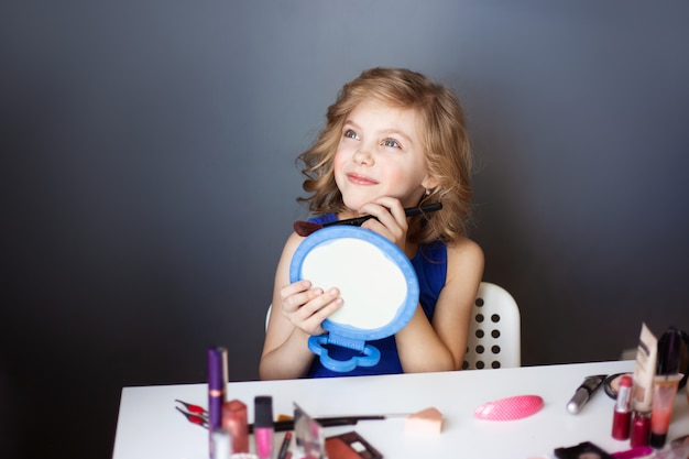 Photo little girl paints her mother’s face with cosmetics, pensive happy girl