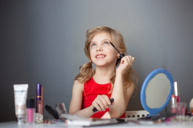 little girl paints her mother’s face with cosmetics, pensive happy girl