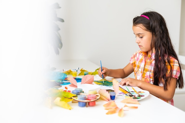 little girl paints leaves with brush at home, autumn art.