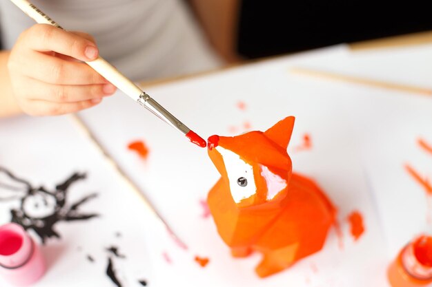 A little girl paints a toy fox made of clay DIY concept
