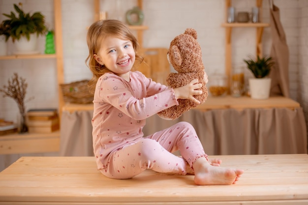 little girl in pajamas holds teddy bear at home in the kitchen