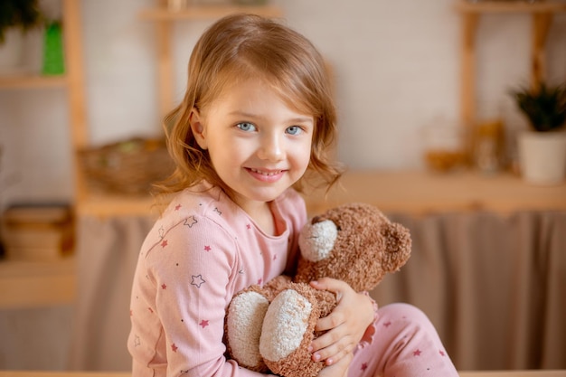 Photo little girl in pajamas holds teddy bear at home in the kitchen