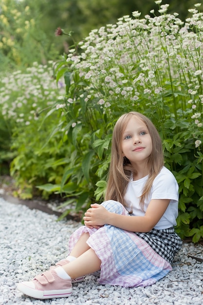 Little girl in the park on a summer day near a flower bed.