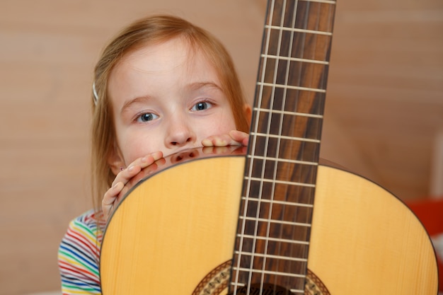 little girl peeks out from behind a guitar case at home.