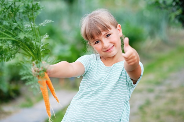 庭でニンジンを選ぶ少女。秋の野菜の収穫。