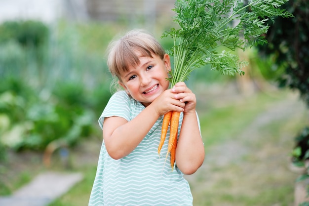 庭でニンジンを選ぶ少女。秋の野菜の収穫。