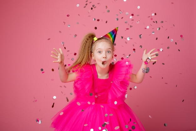 ピンクの背景に紙吹雪を吹く少女が彼女の誕生日を祝う