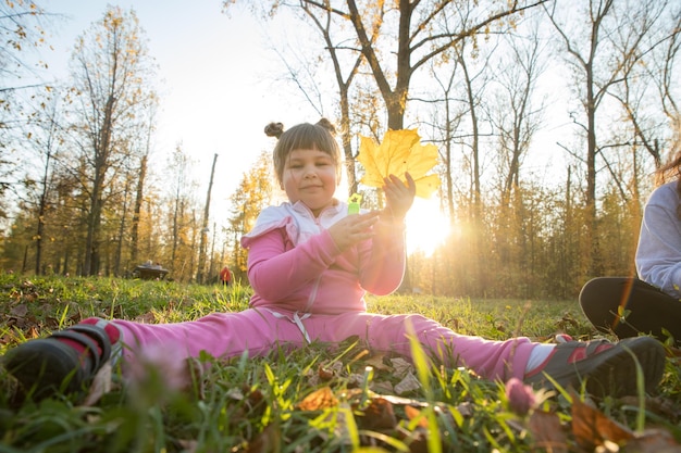 Una bambina in costume rosa seduta per terra nel parco autunnale e con in mano una grande foglia