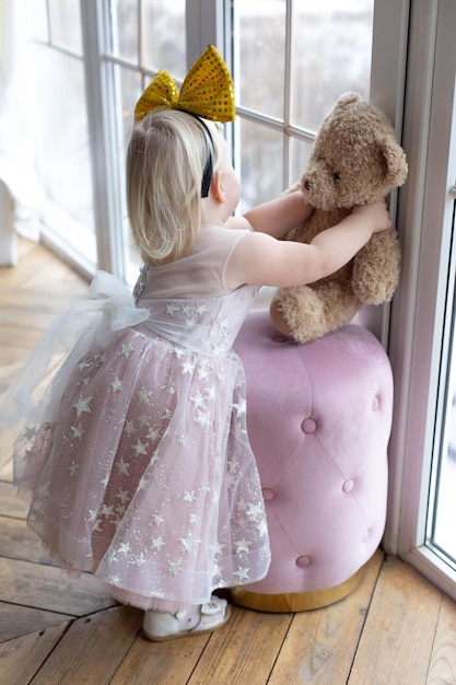 A little girl in a pink dress is hugging a teddy bear.