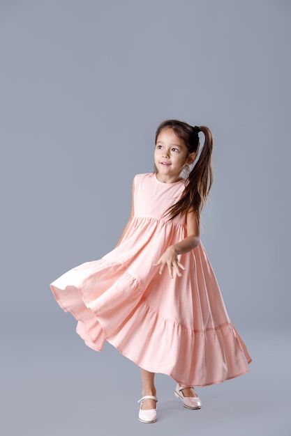 Little girl in pink dress posing on gray background