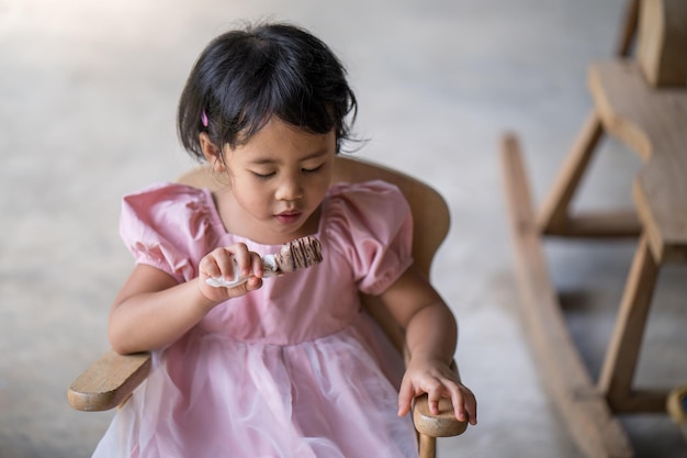 A little girl in a pink dress sits in a wooden chair.