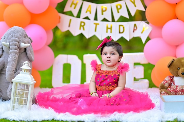 a little girl in a pink dress sitting in front of a banner that says happy birthday