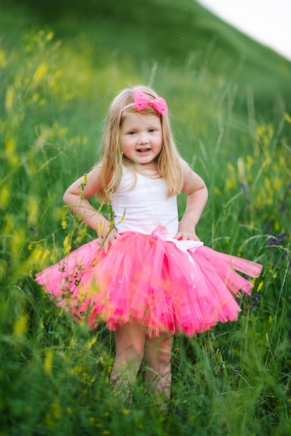 The little girl in a pink dress walks barefoot on the green grass in the field