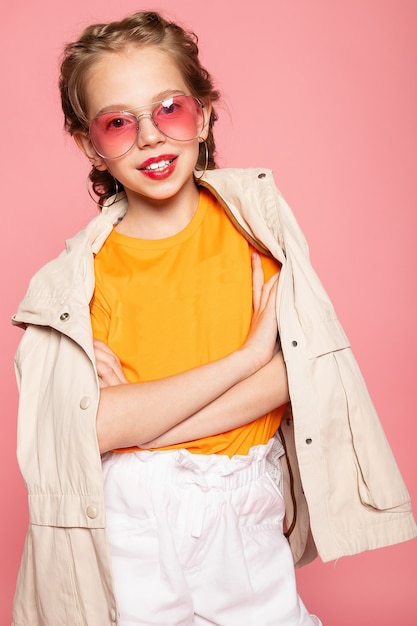 Little girl in pink glasses. Trendy fashion style stylish funtime concept. Vertical full-size full-length portrait of laughing cute sweet adorable lovely charming girl isolated pink wall