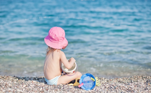 Little girl in pink hat playing with toys on the beach.