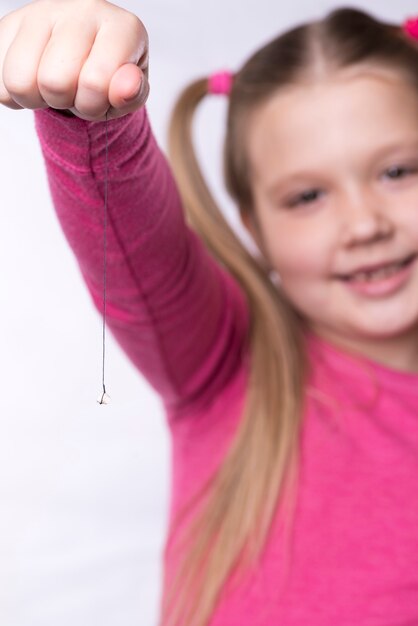 Маленькая девочка в розовом держит на нитке вырванный молочный зуб