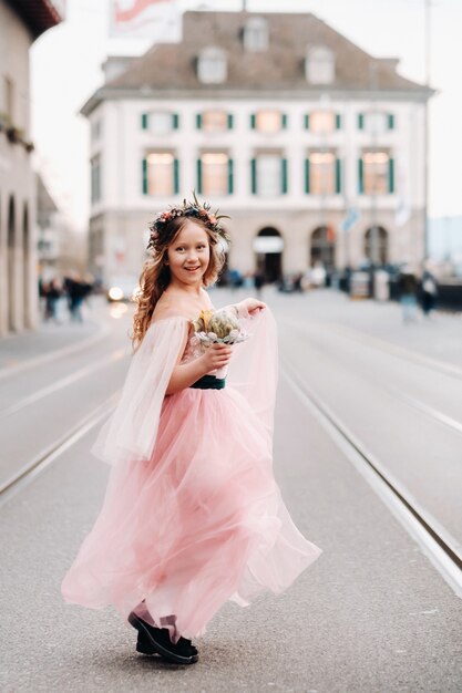 Una bambina in un abito rosa da principessa con un bouquet in mano cammina attraverso la città vecchia di zurigo.ritratto di una ragazza in un abito rosa su una strada cittadina in svizzera.