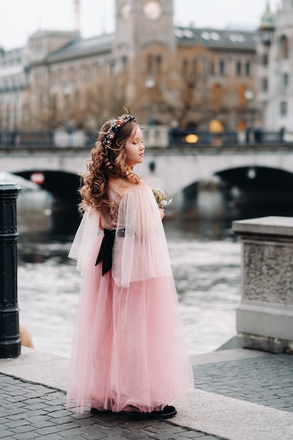 A little girl in a pink Princess dress with a bouquet in her hands walks through the old city of Zurich