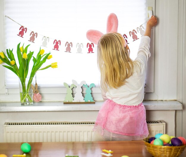 Little girl in pink rock and white shirt decorating room for easter preparation for happy easter