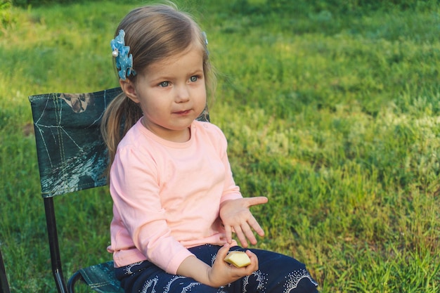 Little girl in pink sitting on chair outdoor. Summer picnic