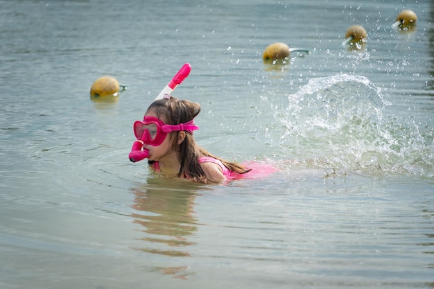 Foto una ragazzina in costume da bagno rosa e uno snorkel con una maschera da immersione nuota sul lago