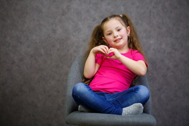 Little girl in a pink t-shirt is sitting on a gray chair. Emotional photo of a child