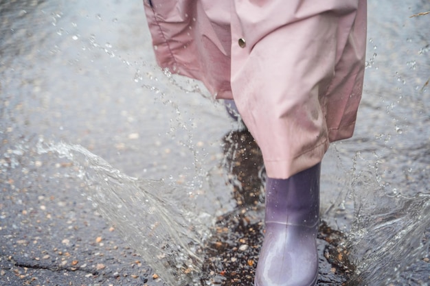 Bambina in impermeabile rosa impermeabile stivali di gomma viola salti divertenti attraverso le pozzanghere sulla strada in una giornata piovosa primavera autunno divertimento per bambini dopo la pioggia attività ricreative all'aperto