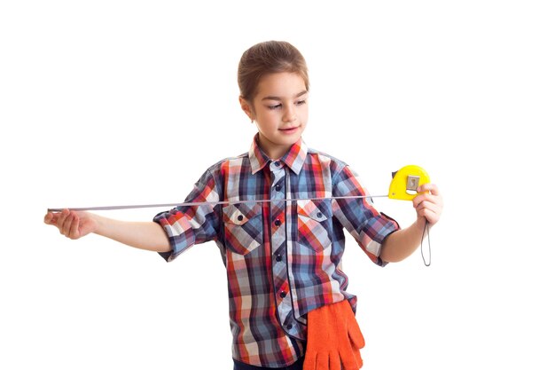 Little girl in plaid red shirt with orange gloves and glasses holding screwdriver and roulette