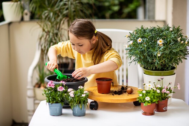 小さな女の子がバルコニーに花を植え、植物の世話をします