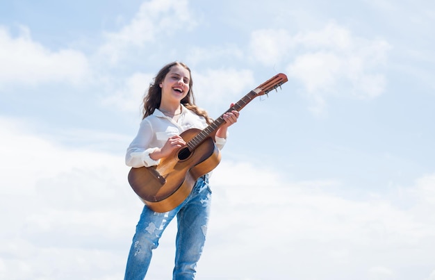 Little girl play guitar she loves music music school classes small guitar player on sky background country music style string musical instrument play on acoustic guitar