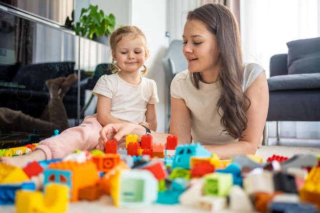 little girl play with constructor toy on floor in home with mom or woman babysitter educational game family at home spend leisure activities time together concept