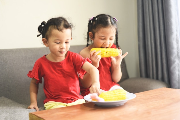 Little girl playing and eating corn at home, Asian cute girl happy kids food concept