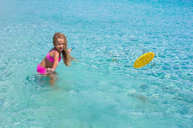 Little girl playing frisbee on tropical white beach during vacation