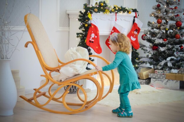 Маленькая девочка играет в комнате с рождественскими украшениями в кресле-качалке