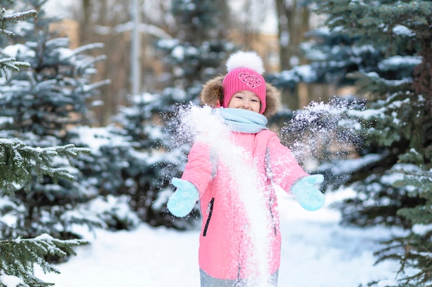 Little girl playing snow, snowballs having fun in winter. happy child enjoying snowflake. Wintertime play for children