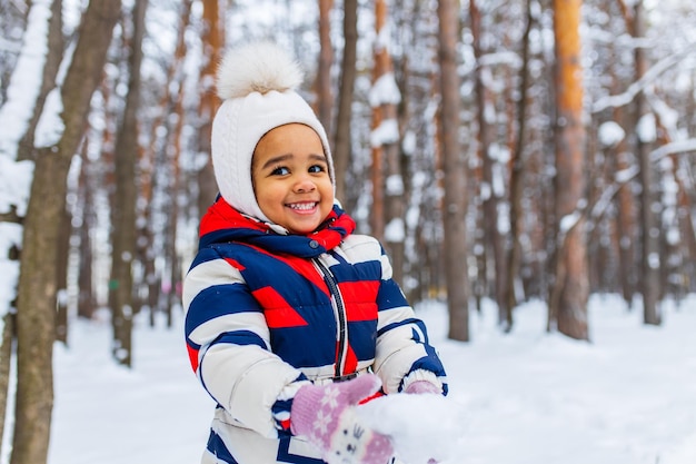 Маленькая девочка играет в снежный зимний день в парке, катаясь на санках с холма