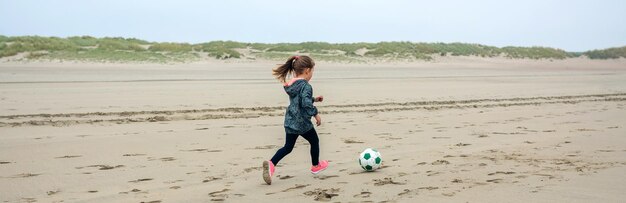 가을 해변에서 축구를 하는 어린 소녀