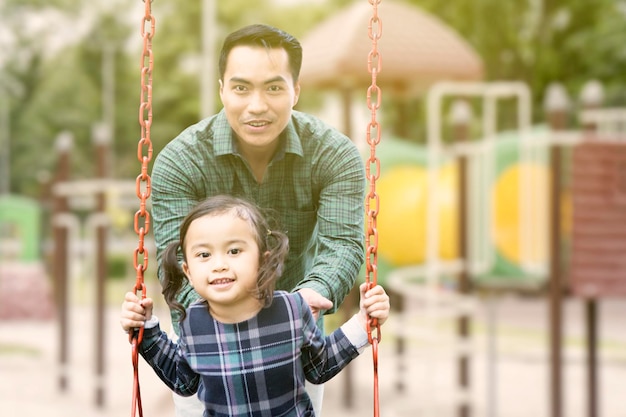 Little girl playing on a swing with her father