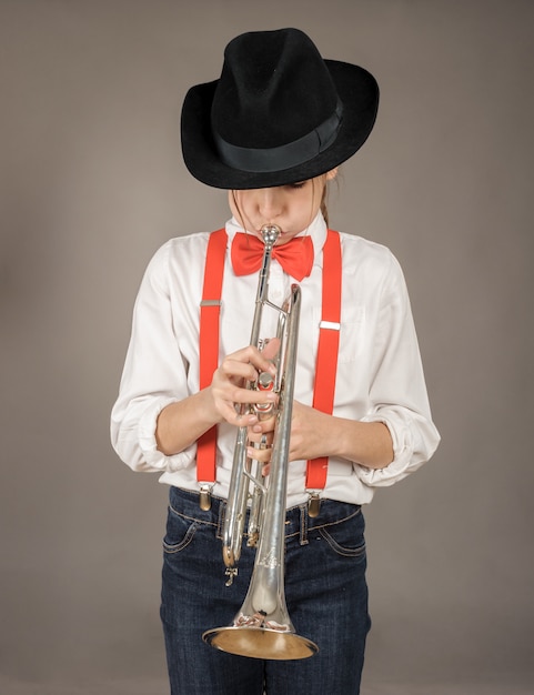 Little girl playing trumpet on gray