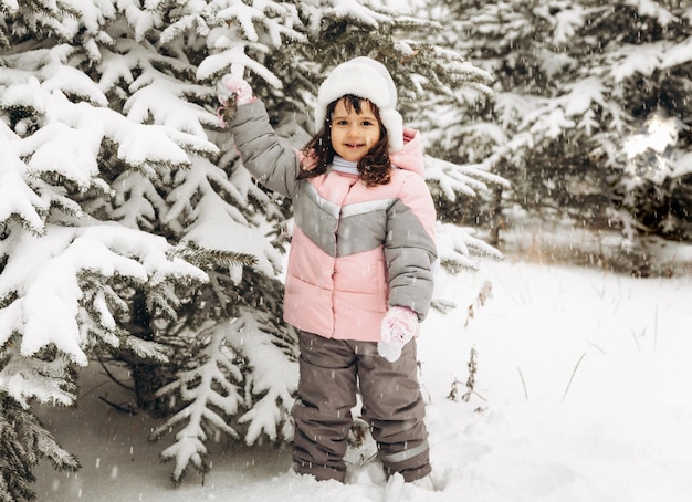 雪の森で冬に遊ぶ少女。美しい冬の子供の肖像画。幸せな子、屋外で冬の楽しみ。