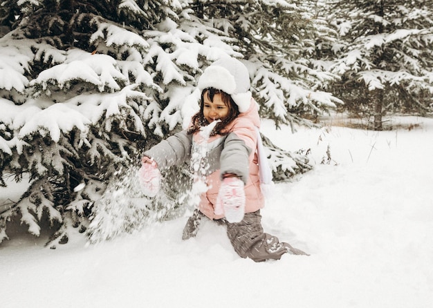 눈 덮인 숲에서 겨울에 노는 어린 소녀. 아름 다운 겨울 아이 초상화입니다. 행복 한 아이, 겨울 재미 야외.