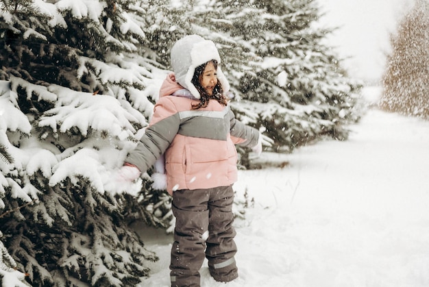 雪の森で冬に遊ぶ少女。美しい冬の子供の肖像画。幸せな子、屋外で冬の楽しみ。